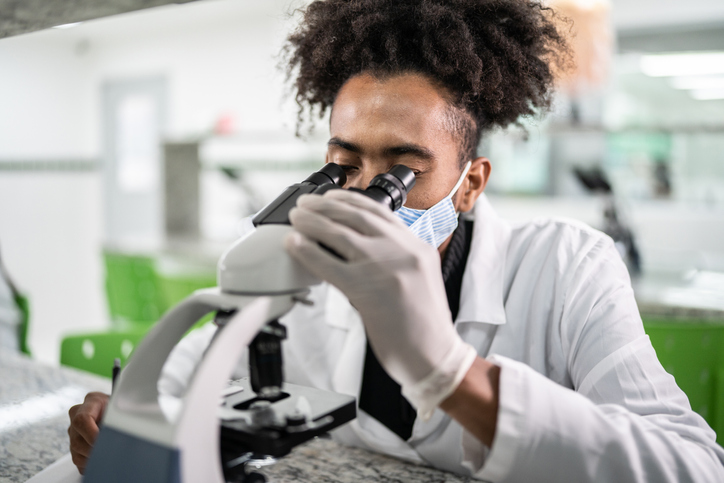 Young man using microscope in the laboratory - using a face mask