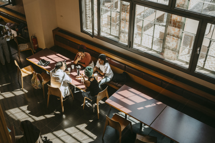 Teacher with female students discussing while sitting in college cafeteria