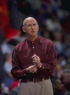 Bald man in red shirt adjusts his watch.