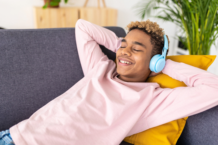 Teenage boy enjoying listening music while relaxing lying on a couch at home.