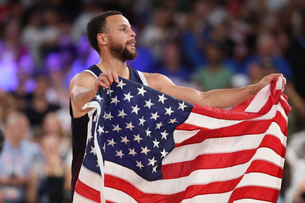 Team USA wins fifth straight gold, defeating France 98-87 in Paris // Steph Curry with US flag at Paris Olympics - GettyImages