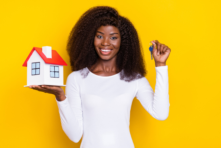 Portrait of cheerful pretty lady hand hold demonstrate little house key isolated on yellow color background